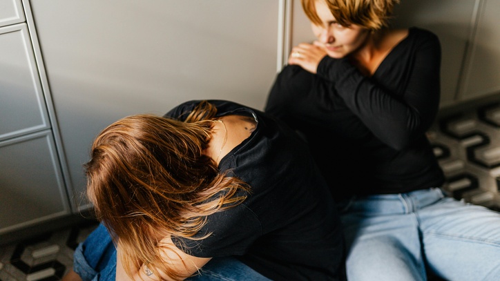 Zwei Frauen sitzen auf dem Boden. Die eine tröstet die andere Frau.